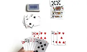 Karty do gry, w tym ręka z kartami 4, 8, 2, 3, 4, 7, 10, oraz stosy kart, w tym króle i damy. Ktoś gra w karty, ale czy jest dobrym graczem, czy tylko dureń?