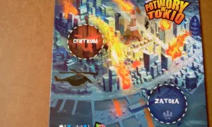 Ilustracja gry planszowej "Potwory w Tokio" z płonącym miastem, wieżą Eiffla i helikopterem.