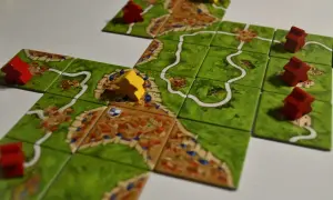 Rozgrywka w Carcassonne: czerwoni i żółci rycerze zajmują pola z miastami i drogami, budując średniowieczny krajobraz.