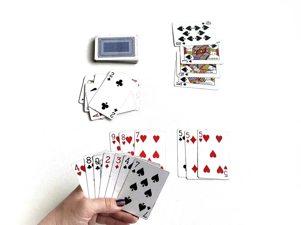 Karty do gry, w tym ręka z kartami 4, 8, 2, 3, 4, 7, 10, oraz stosy kart, w tym króle i damy. Ktoś gra w karty, ale czy jest dobrym graczem, czy tylko dureń?