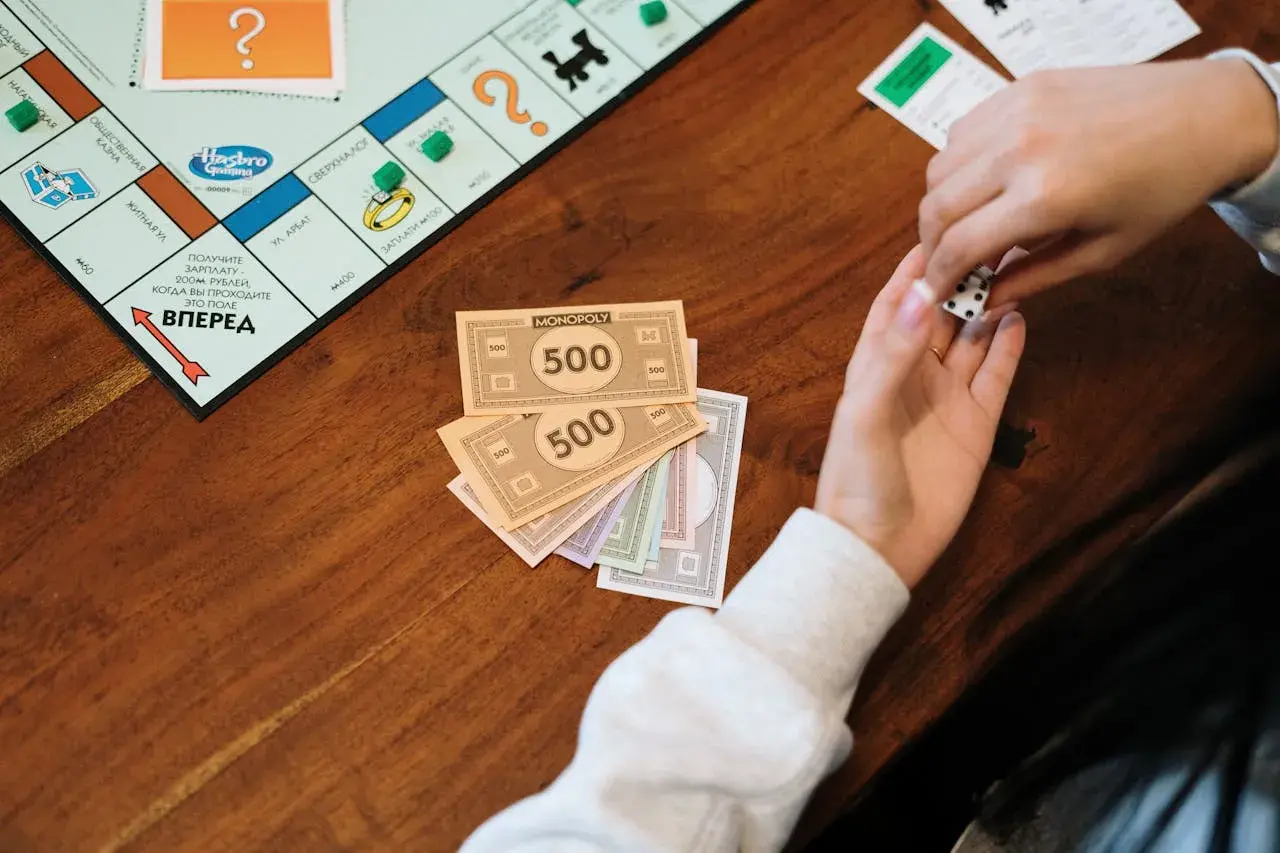 Ręce trzymają kości i pieniądze z gry Monopoly. Naucz się, jak rozdawać pieniądze w Eurobiznes, by wygrać!