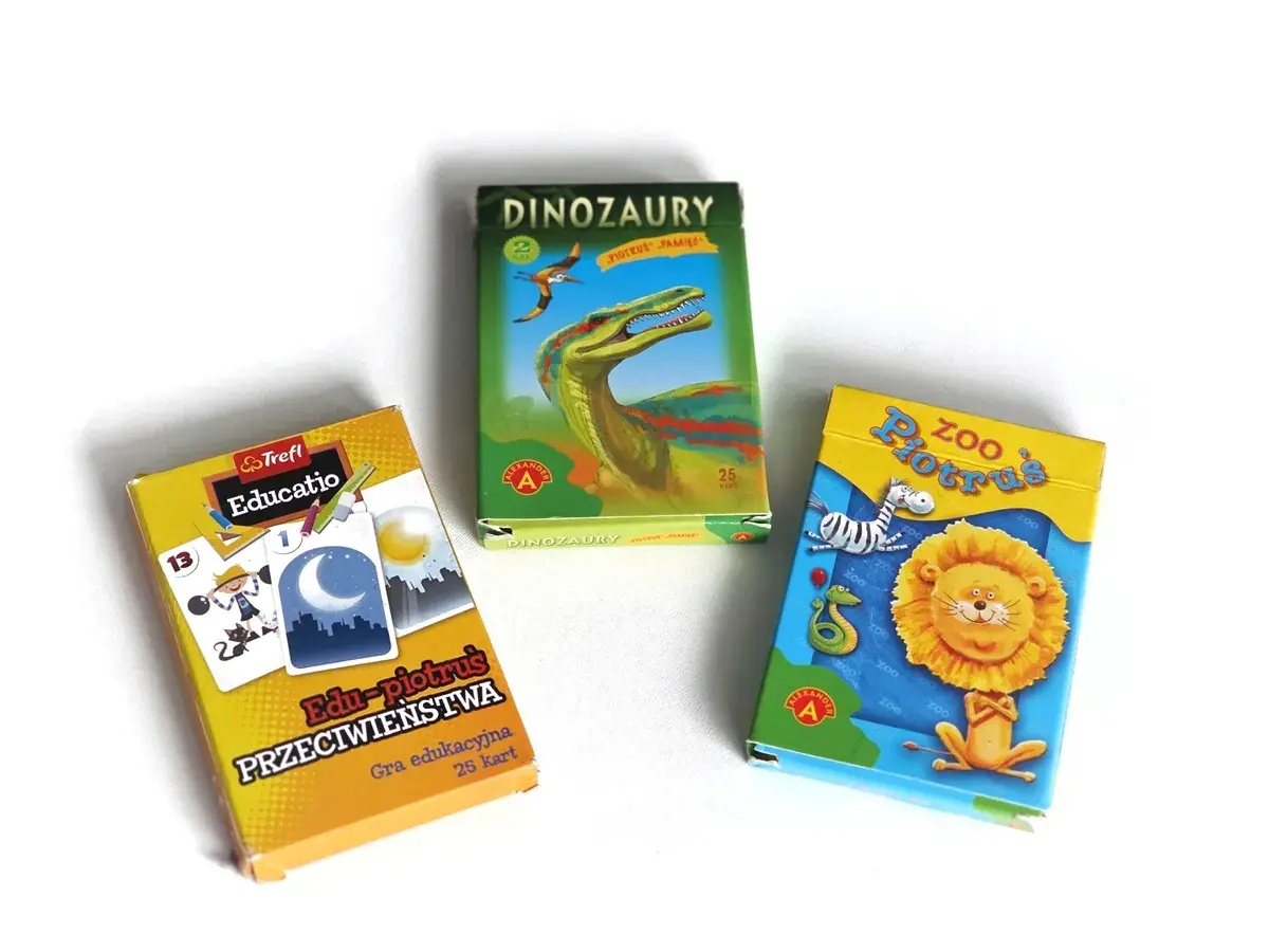 Trzy pudełka z grami karcianymi: "Dinozaury Piotruś", "Zoo Piotruś" i "Edu-piotruś Przeciwieństwa".